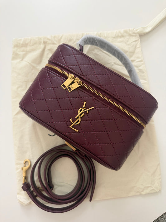 Maroon handbag with gold zipper on a beige fabric background
