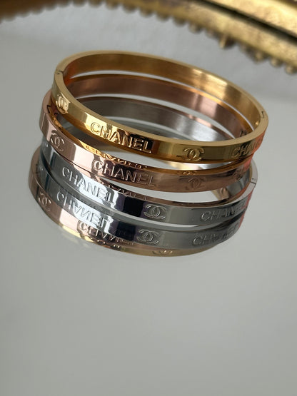 Three Chanel bangles in gold, rose gold, and silver on a light gray background