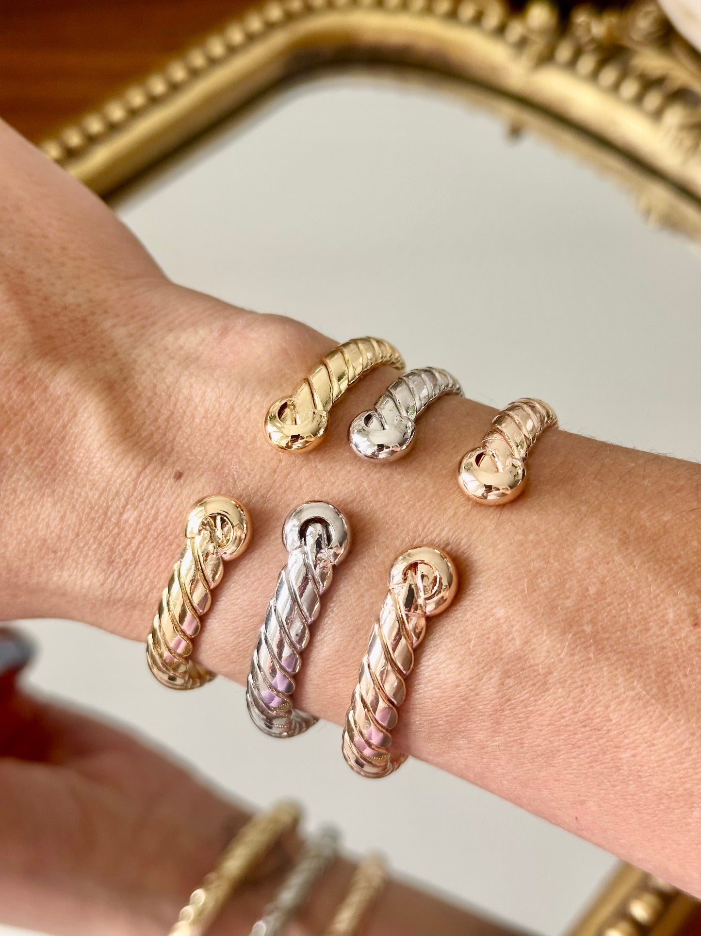 Close-up of a wrist wearing multiple gold and silver bracelets with a decorative mirror in the background.