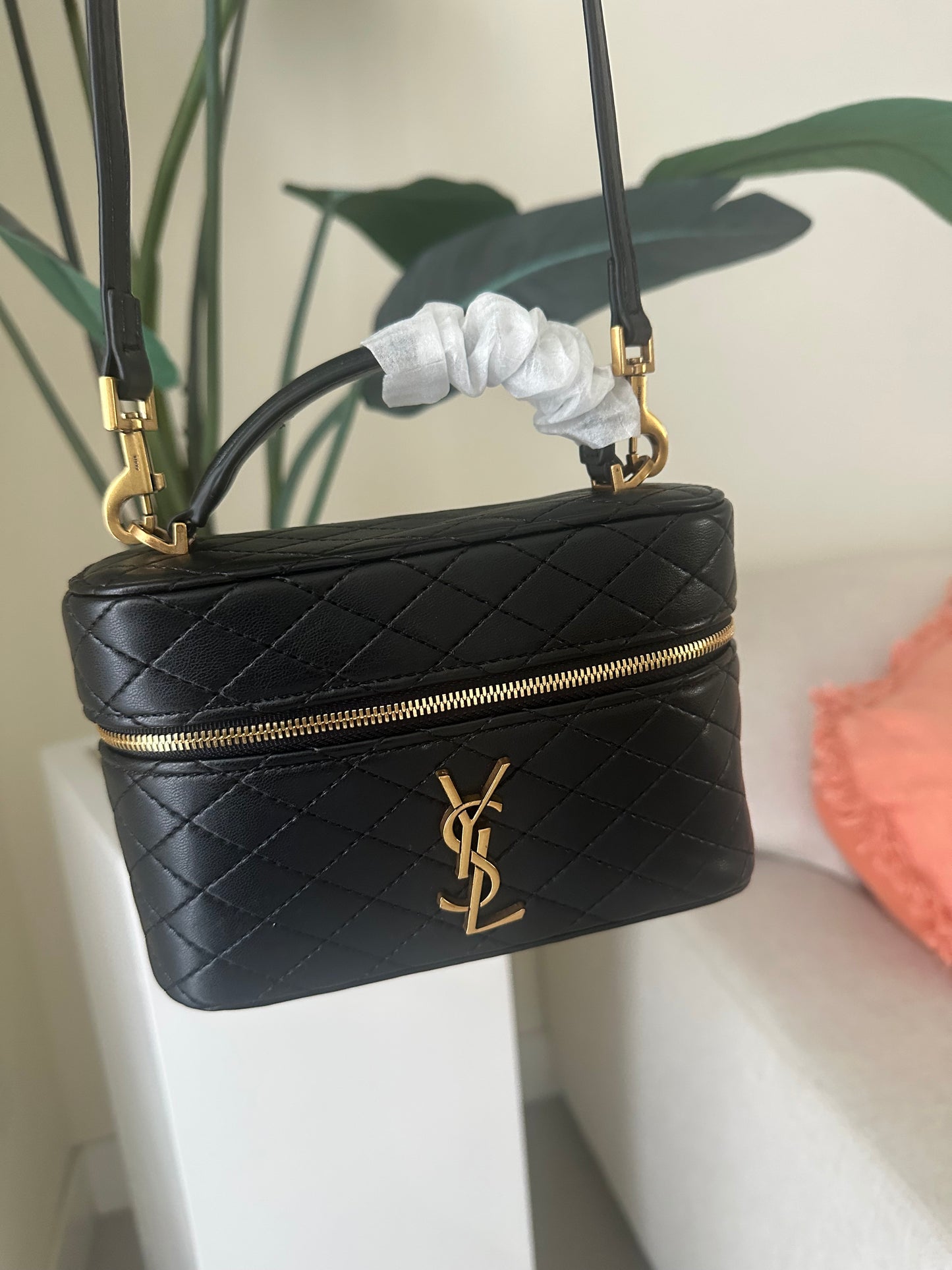 Black quilted handbag with gold zipper and YSL logo on a white surface.